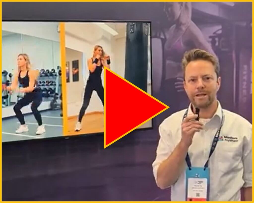 Monitors AnyWhere representative presenting at ISE 2026 with a screen showing a gym workout use case powered by custom digital signage application.